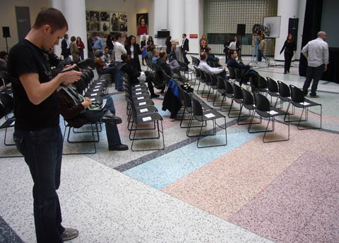 Young photographer inspects camera as he stands alongside a sea of mostly-unfilled chairs