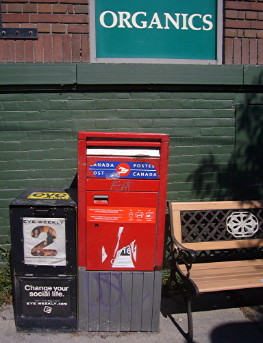 ‘Eye Weekly’ box, mailbox, and bench under ORGANICS sign