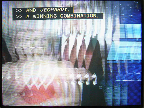 Jittery, fragmented TV image has clear captioning reading AND JEOPARDY. A WINNING COMBINATION
