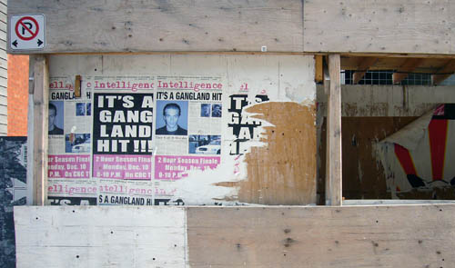 Decaying posters on construction hoarding read Intelligence IT’S A GANGLAND HIT!