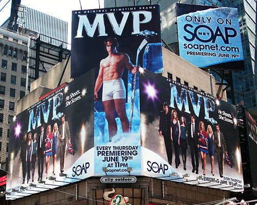 Billboards for ‘MVP’ cover two sides of a Times Square building, with tall billboard attached square on the corner showing a shirtless guy with a hockey stick