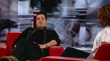 Strombo, hands in pockets, leaning back in chair in unzipped black sweather