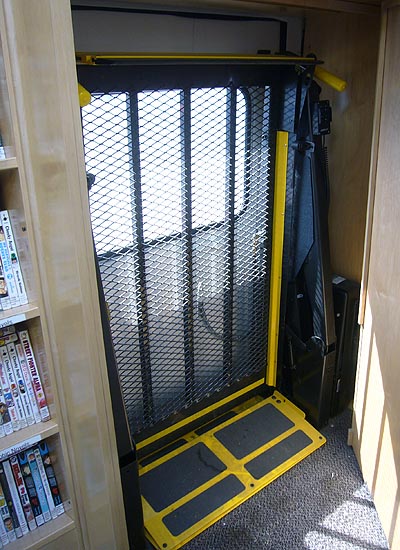 Corrugated metal wheelchair lift, with yellow safety edges, sits folded upright inside wall recess