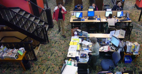 Overhead view shows librarians&rsquo; desk, staircase off to the left, and long table of computer workstations all on top of green floral carpeting