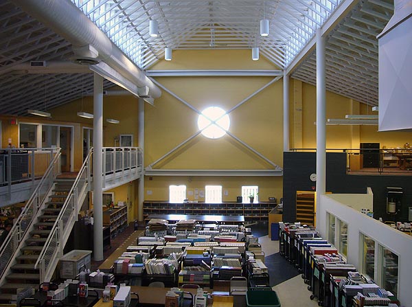 Yellow wall sits at and of large atrium, with white pipes lining a vaulted barn-like ceiling