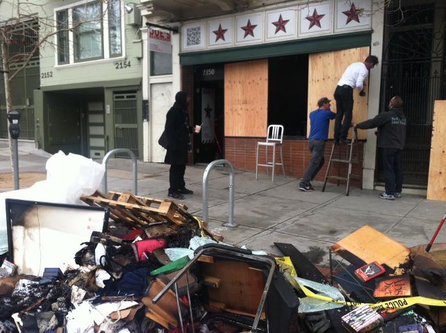 Boarded-up storefront and charred debris out on sidewalk