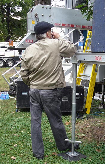 Grey-haird man in bomber jacket, jeans, and newsboy cap has back to camera