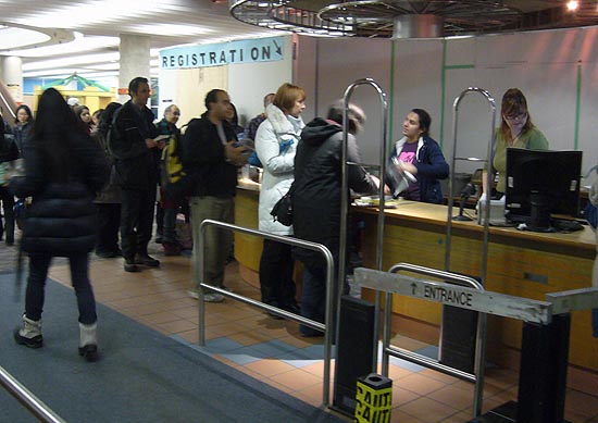 Queue of patrons at checkout desk, behind which is an expanse of drywall