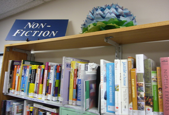 Paper chrysanthemum sits on top of bookshelf alongside NON-FICTION sign