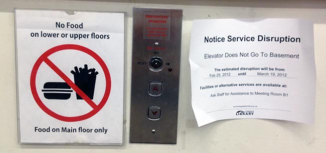 Frayed paper signs taped on either side of elevator buttons