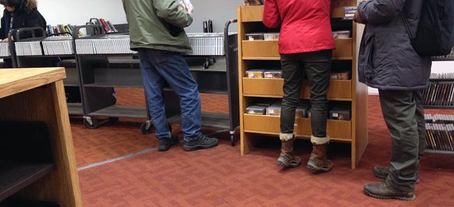 People paw through DVDs on trucks and on one wooden shelf