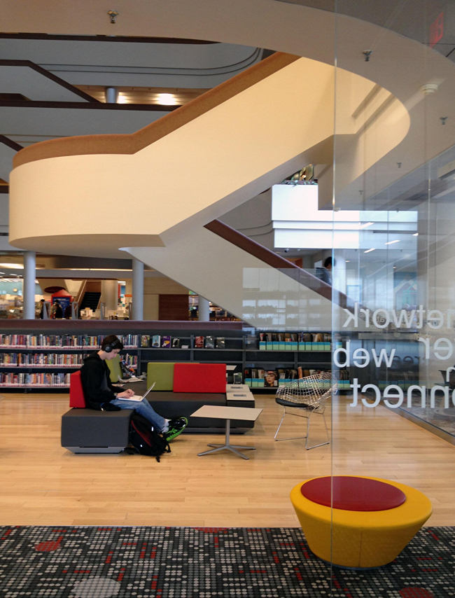 Man works at laptop while seated on colourful benches under staircase