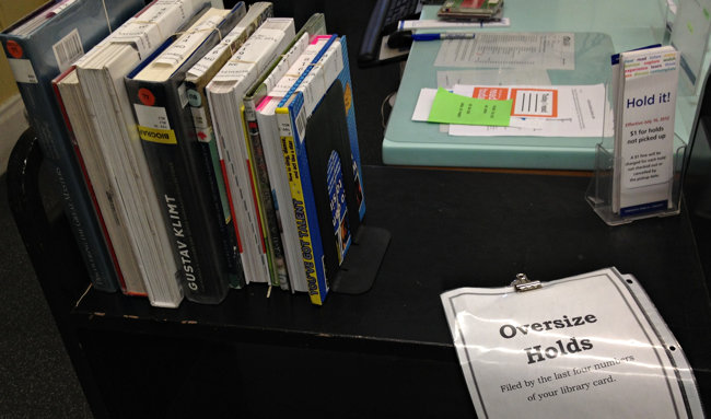 Cart with a couple of items on it and taped-on Oversized Holds sign