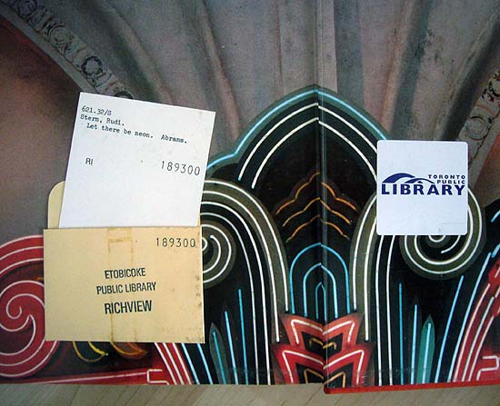 Circulation card for ‘Let There Be Neon’ peeking out of Etobicoke Public Library pocket. On obverse page, RFID sticker