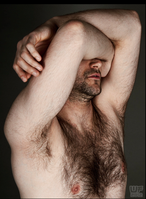 Hirsute man holds right arm crossed over his eyes, left arm resting on the right