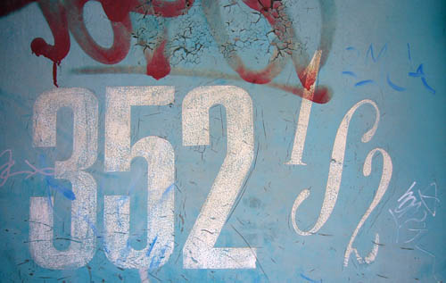 Decayed painted-on numbers on a graffitied door read 352½, with the ½ a 1, an ∫, and a 2