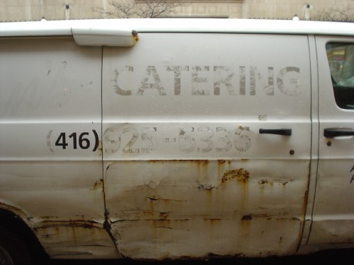 Side of beaten-up van has barely-visible type in Frutiger reading CATERING and a phone number, with clearly visible 416)
