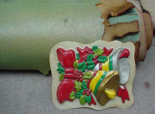 Extruded plastic tray, with a Christmas-bell design, leans against rolled-up carpet