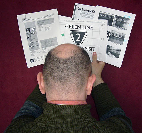 Facing a cranberry-coloured background, I hold up a schematic of TTC signage, a printout reading GREEN LINE and the number 2 in a keystone, a magazine article, and a page of printouts of photos, including a sign reading Bessarion
