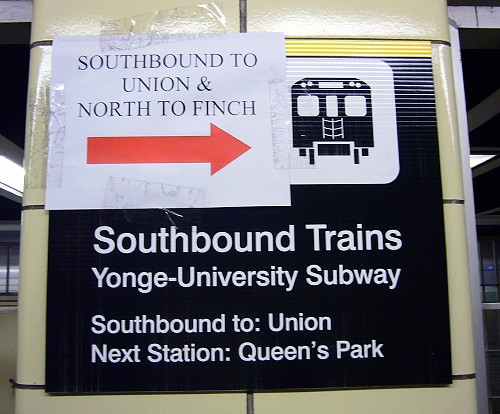 Printed sign says Southbound Trains Yonge-University Subway, with a laser-printed sign with a huge red arrow taped onto it reading SOUTHBOUND TO UNION & NORTH TO FINCH