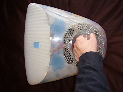 Hand grasps the handle of an iMac with a blue Apple logo and sublimated blue daisy-shaped decorations