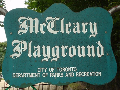 Green sign with undulating edges reads McCleary Playground in blackletter and CITY OF TORONTO DEPARTMENT OF PARKS AND RECREATION in Helvetica Condensed
