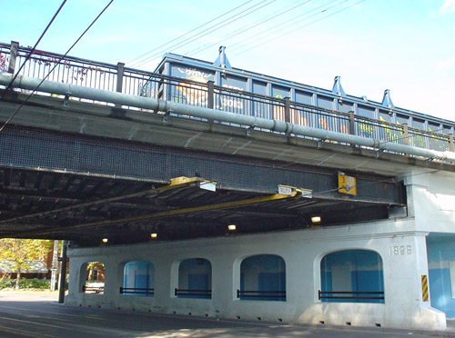 A train’s freight car sits atop a plaster-covered white overpass at an angle to a city street
