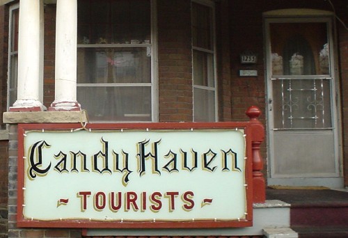 Handmade sign on porch of house reads Candy Haven in blackletter and TOURISTS in sansserif