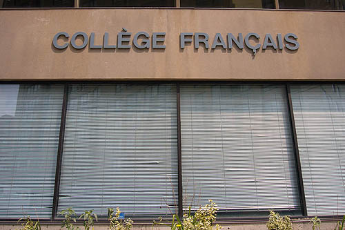 Letters on concrete wall above Venetian-blind-covered windows read COLLÈGE FRANÇAIS