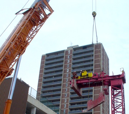 Orange crane hoists large steel panel to platform of stationary crane