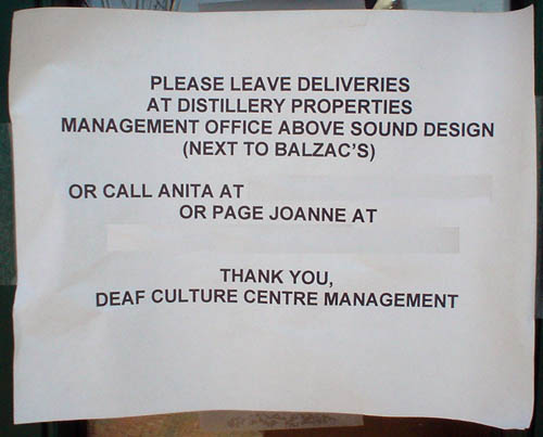 Sign in Arial reads PLEASE LEAVE DELIVERIES AT DISTILLERY PROPERTIES... OR CALL ANITA AT [blanked] OR PAGE JOANNE AT [blanked] THANK YOU, DEAF CULTURE CENTRE MANAGEMENT