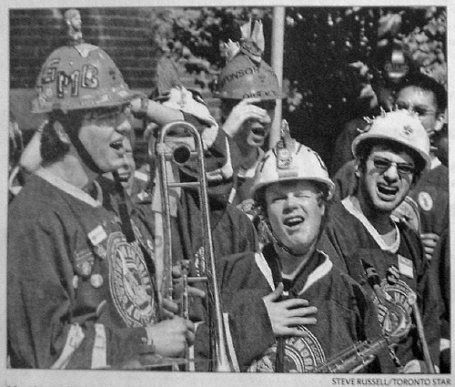 Young guys in hardhats and hockey jerseys, one holding a trombone