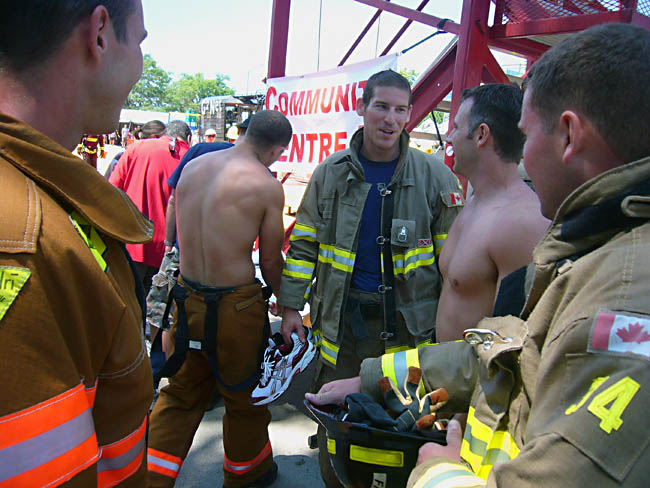 Five firemen, two of them shirtless, standing around talking