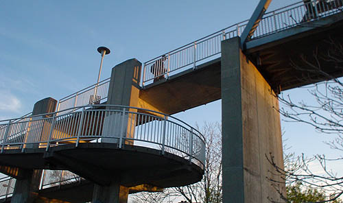 Concrete footbridge seen at twilight has a winding downward ramp on one end