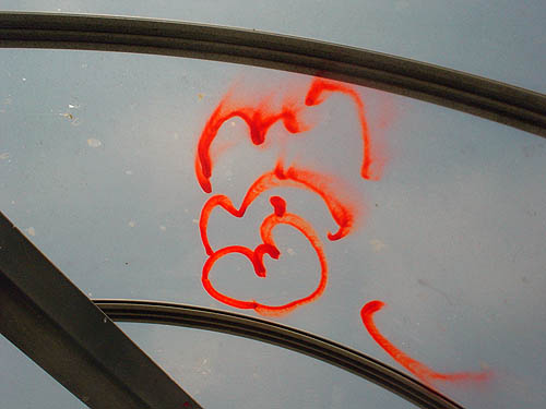 Four squiggles of neon-orange spraypaint on curved clear plastic roof