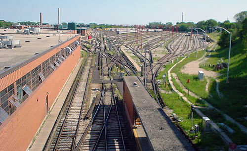 Groups of train tracks spread out in three directions alongside a long red-brick building with opened windows