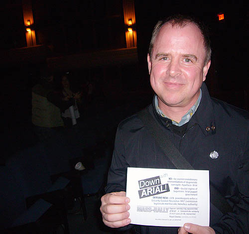 In a darkened theatre, Gary Hustwit grins and holds a Down with Arial! handbill