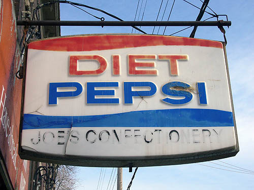 Sign reading DIET PEPSI and, in worn-out letters, JOE’S CONFECTIONERY, with red and blue wavy stripes