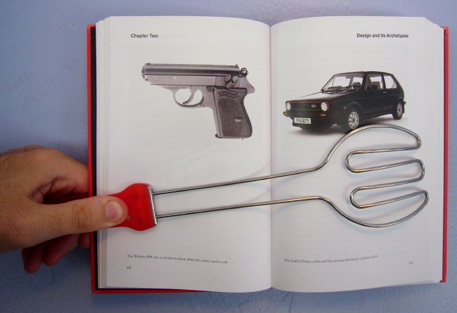 Red-handled steel tongs hold a book open showing a Walther PPK pistol and Golf GTI, both black with tiny red accents