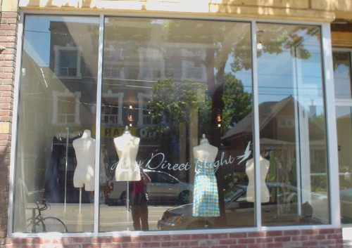 Store window shows mannequins in dresses and camisoles and the words Any Direct Flight in script