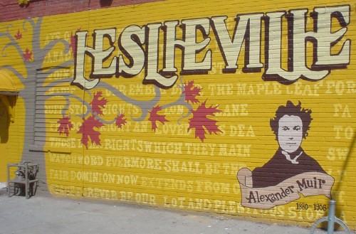 Yellow wall mural reads LESLIEVILLE and shows many lines of text, a maple tree, and a likeness of Alexander Muir
