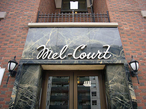 Metal cursive letters on stone entranceway read Mel-Court