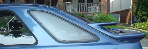 Blue car has an angled-forward rear quarter window and two stacked spoilers attached to the rear window