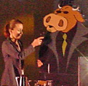 Giant cutout of bull in a black duster speaks into microphone onstage