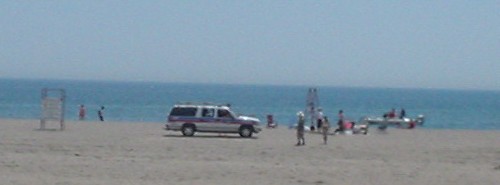 White Suburban with red and blue stripes sits alongside a few people on a distant beach