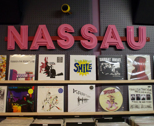 Pink letters made of ever-smaller stacks read NASSAU over a display of vinyl albums