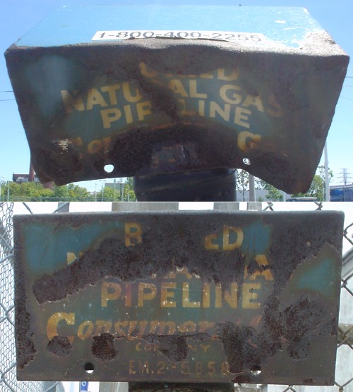 Two rusty, dented signs on poles warning of buried natural-gas pipelines
