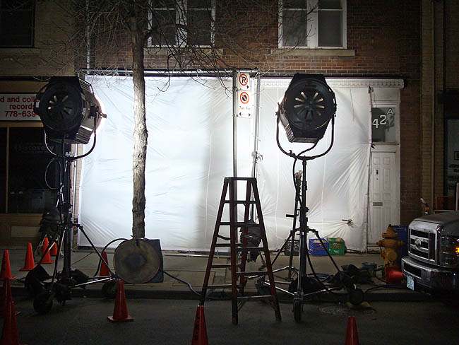 Klieg lights illuminated a dropcloth-draped storefront during a nighttime movie shoot