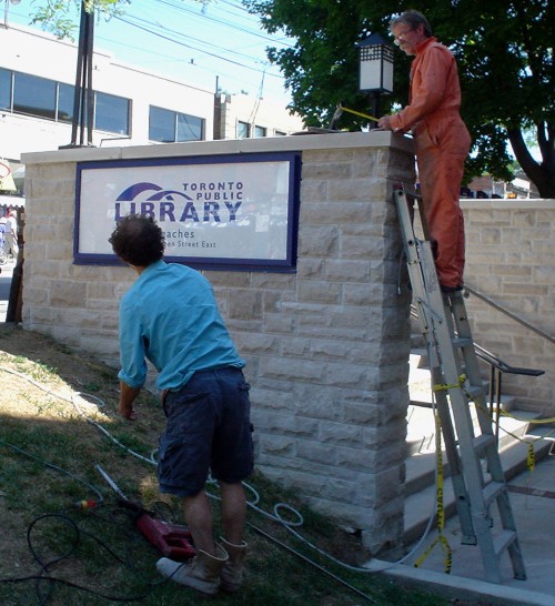 Workman on ladder leaning against retaining wall talks to other man