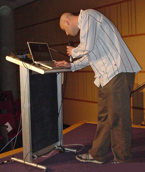 Dean Jackson leans to inspect PowerBook at podium